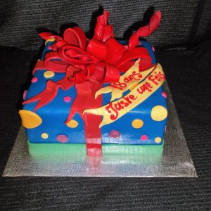 Gâteau en pâte de sucre en forme de cadeau. Décoré d'un ruban et d'un chou rouge, avec des pois jaunes et roses.