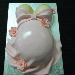 Gâteau en pâte de sucre en forme de ventre de maman portant une robe rose. Décoré de jolies fleurs roses. Parfait pour un shower de bébé.