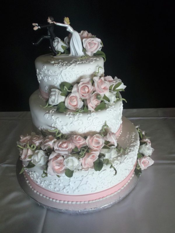 Gâteau de mariage 3 étages blanc et rose. Avec rose en pâte de sucre et silouhette de la mariée qui agrippe le marié en ornement. Fait sur mesure, pour plus d'information contactez-nous.