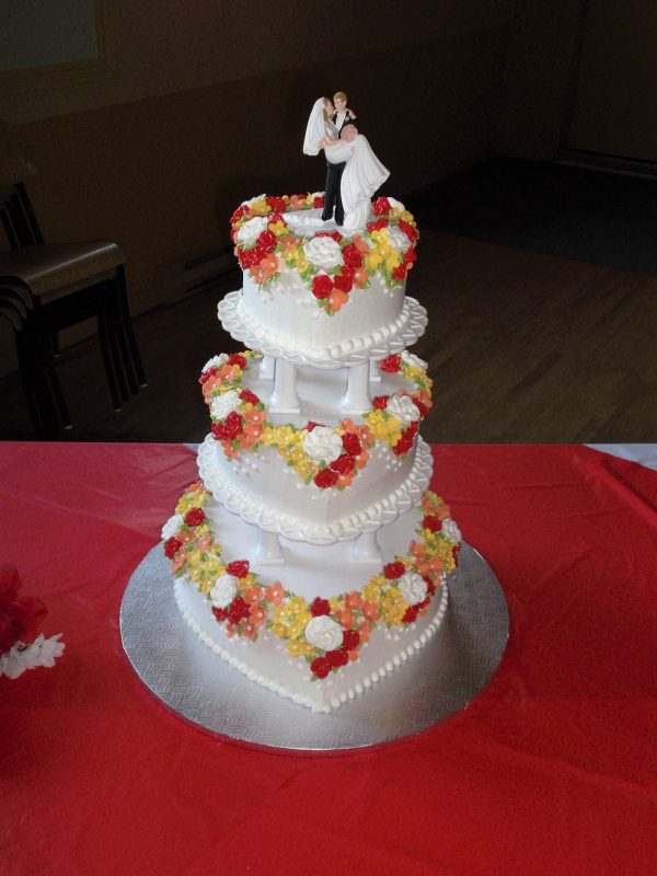 Gâteau de mariage fait sur mesure. 3 étages en forme de coeur sur des pilliers blanc. Orné de fleurs blanches rouge et jaunes. Fait sur mesure, pour plus d'information contactez-nous.