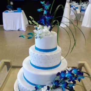 Élégant gâteau de noce blanc et bleu fait en pâte de sucre. Avec décoration de perles et de fleurs bleues. Fait sur mesure, pour plus d'information contactez-nous.